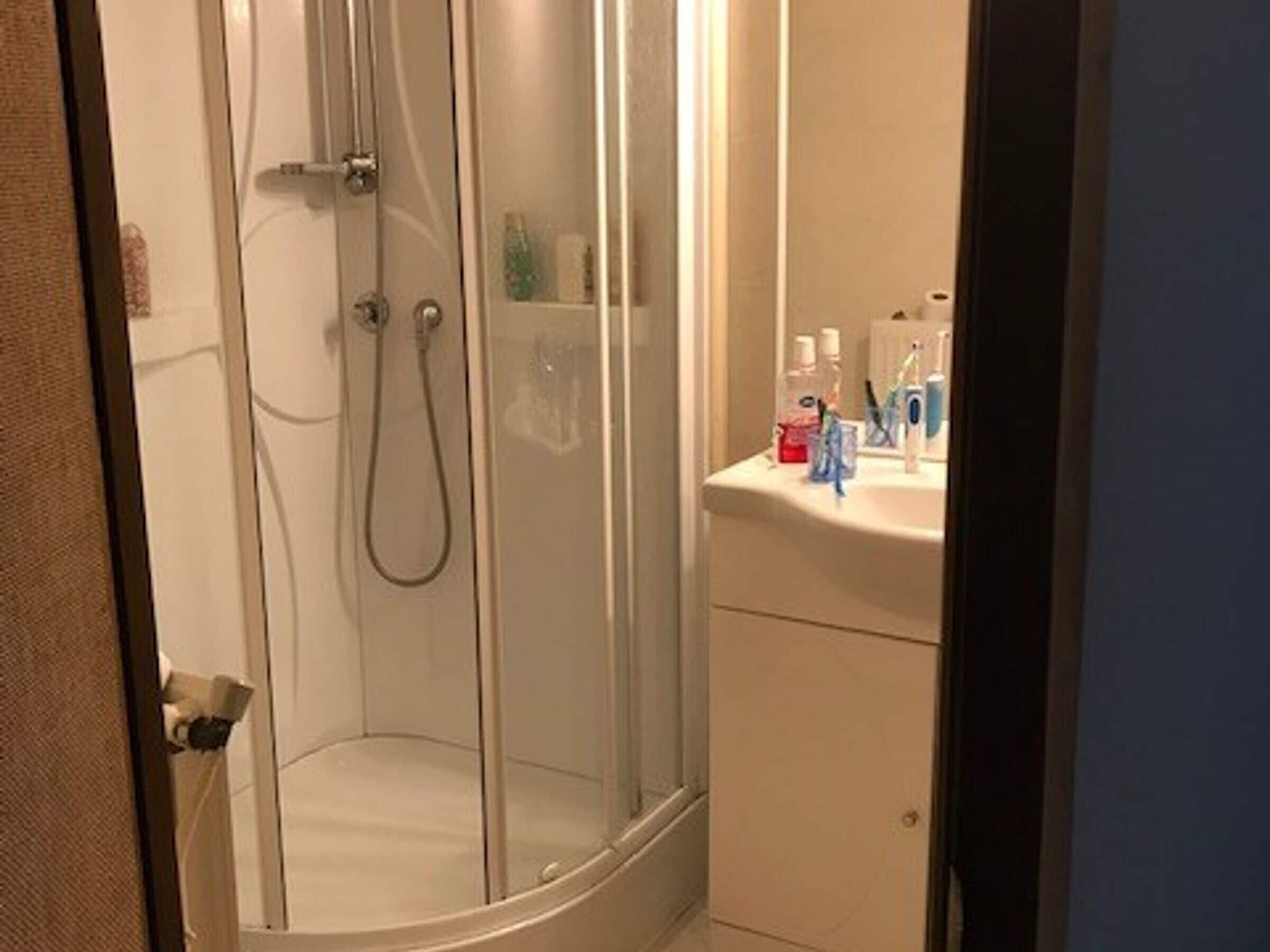 A shower with a glass door, a sink with toiletries, and a cabinet.