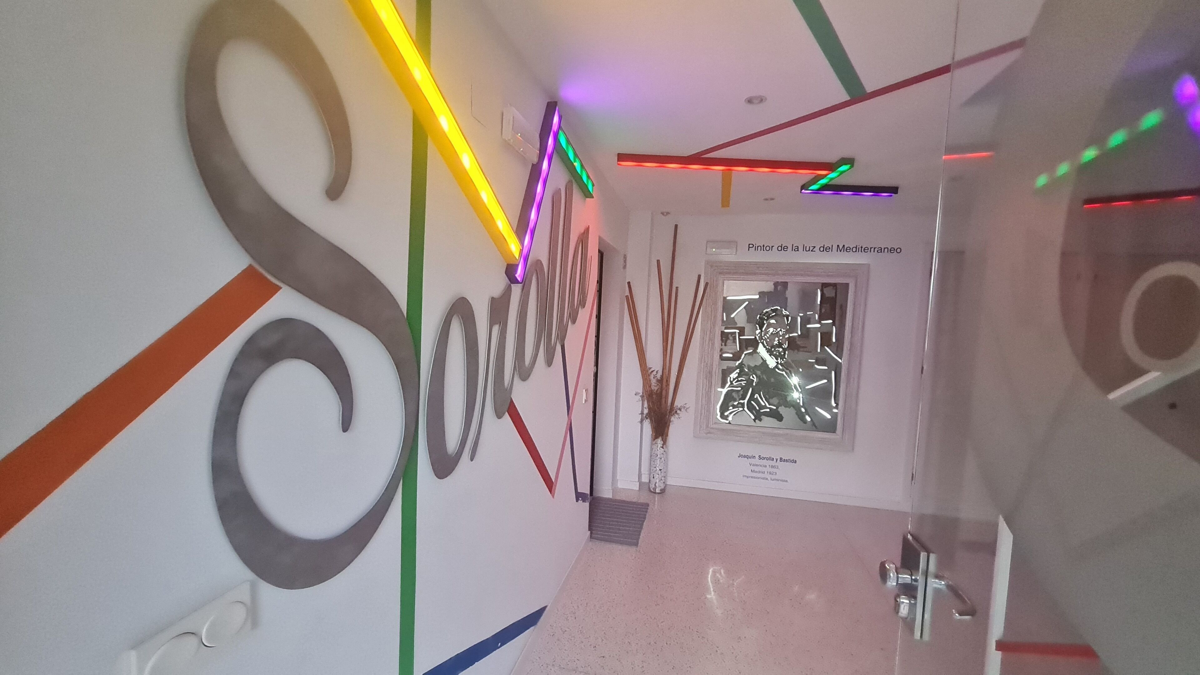 A hallway with a large wall mural, a framed artwork, and a door with a sign.