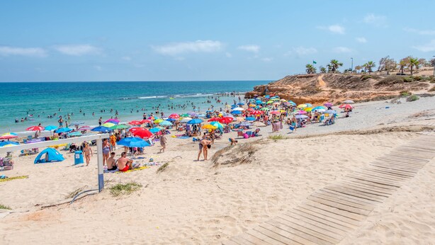 Ein belebter Strand mit vielen bunten Sonnenschirmen und Menschen, die Sand und Wasser genießen.