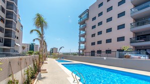 Ein modernes Hotel mit Schwimmbad, mehreren Balkonen und blauem Himmel.