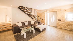 A modern living room with a staircase, a sectional sofa, a glass coffee table, and a stone accent wall.