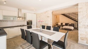 A modern kitchen with white cabinets and a central island, a dining area with a white table and black chairs, and a stone wall separating the kitchen from the living area.