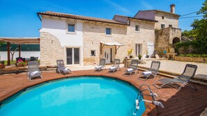 A pool area with lounge chairs and a stone building with a tiled roof.