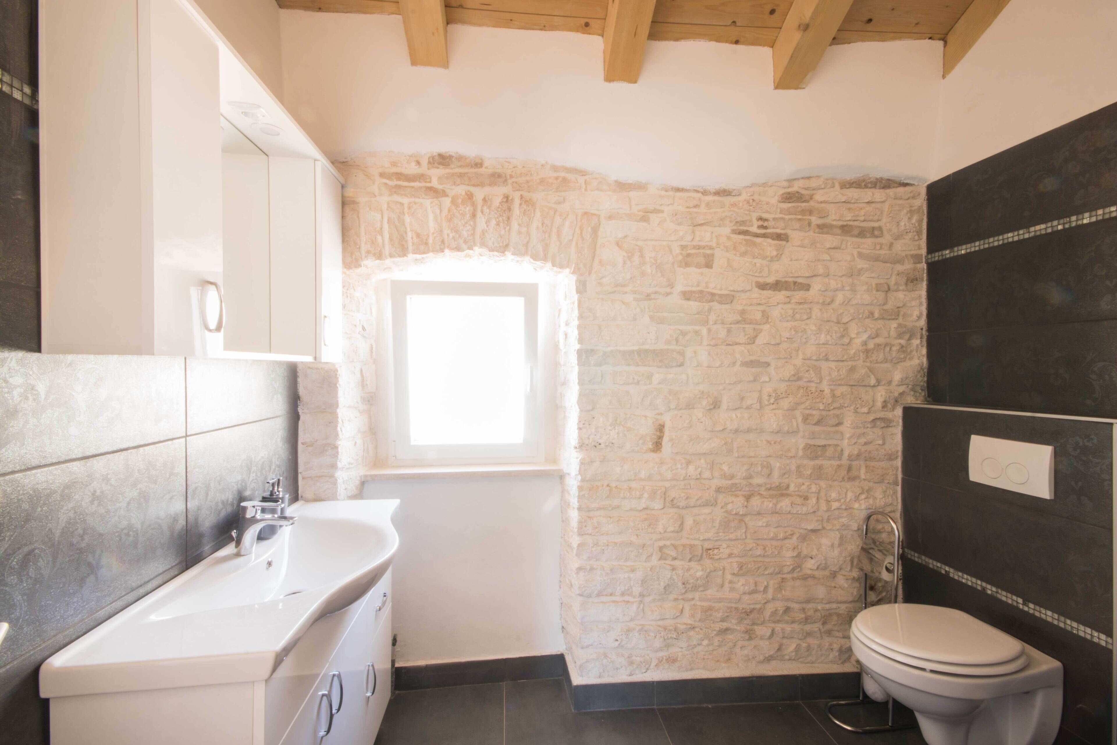 Une salle de bain avec un mur en pierre, un lavabo blanc et des toilettes.