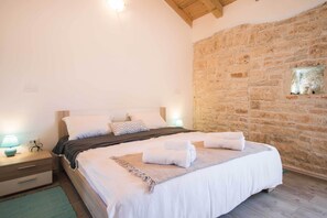 Un dormitorio con una cama grande, una mesita de noche, una lámpara y una pared de piedra.