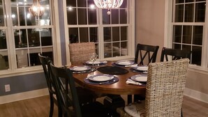 Une salle à manger avec une table ronde dressée pour quatre personnes, entourée de chaises sombres et d’un fauteuil en osier.