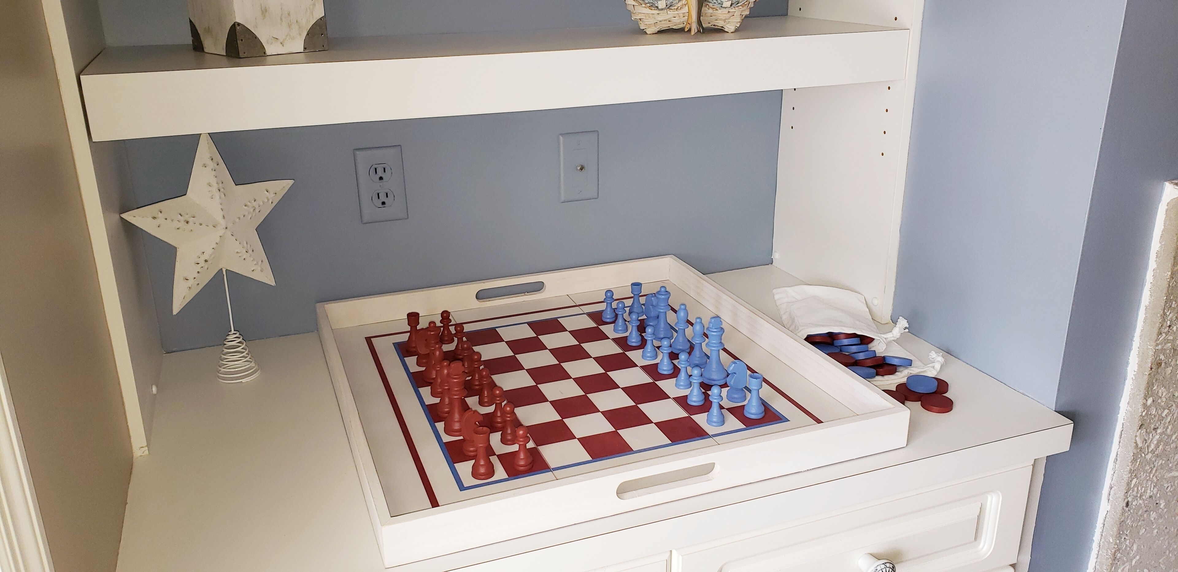 A white dresser with a chessboard and pieces, a star decoration, and a small lamp.