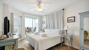 A bedroom with a bed, bedside tables, a ceiling fan, a dresser, and a window with curtains. - Luxury Oceanfront with porch and swing daybed! Pet Friendly w/ fee, Elevator - Seaside Villa 101 (Folly Beach)