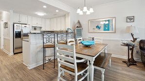 A modern kitchen with white cabinets, stainless steel appliances, and a wooden dining table with white chairs. - Luxury Oceanfront with porch and swing daybed! Pet Friendly w/ fee, Elevator - Seaside Villa 101 (Folly Beach)