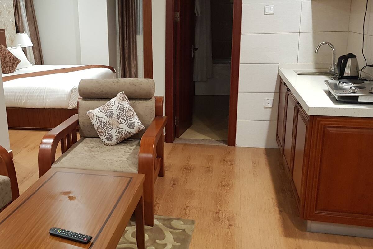 A compact hotel room with a bed, two sofas, a small table, and a kitchenette.