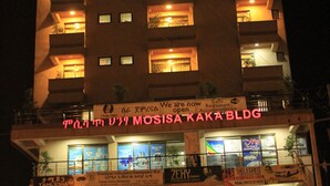 En bygning med flere etager og oplyst skiltning, herunder et tydeligt skilt med "MOSISA KAKA BLDG".