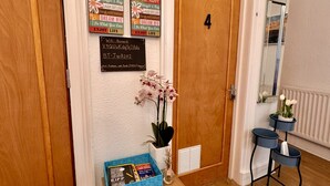 A hallway with a wooden door marked '4', a wall clock, motivational posters, a small table with a vase of flowers, and a blue bookcase. - @part Bernard Rooms (Edinburgh)