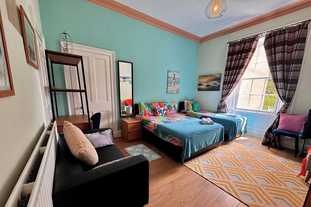 A bedroom with two beds, a sofa, a window with curtains, and a radiator.
