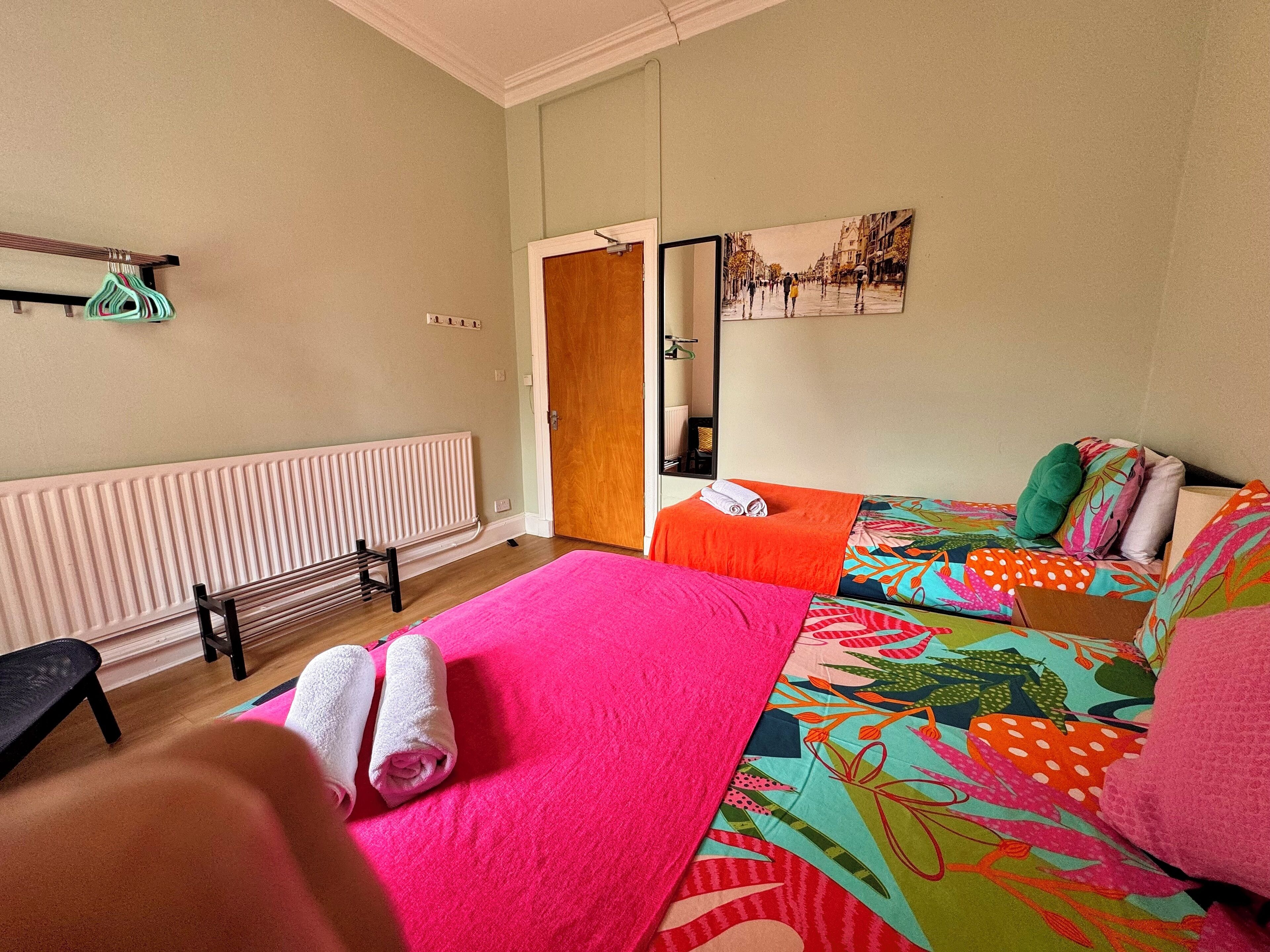 A room with two beds, a bench, a radiator, a mirror, and a door.