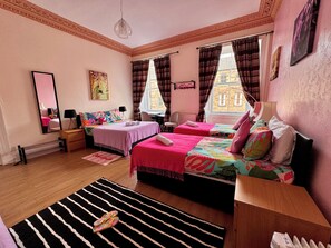 A well-lit bedroom with two beds, a large mirror, a wooden dresser, and a view of a building through the window. - @part Bernard Rooms (Edinburgh)