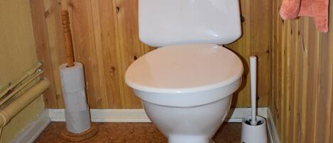 A bathroom with a wooden wall, a toilet, a roll of toilet paper, and a pink towel hanging on the wall.