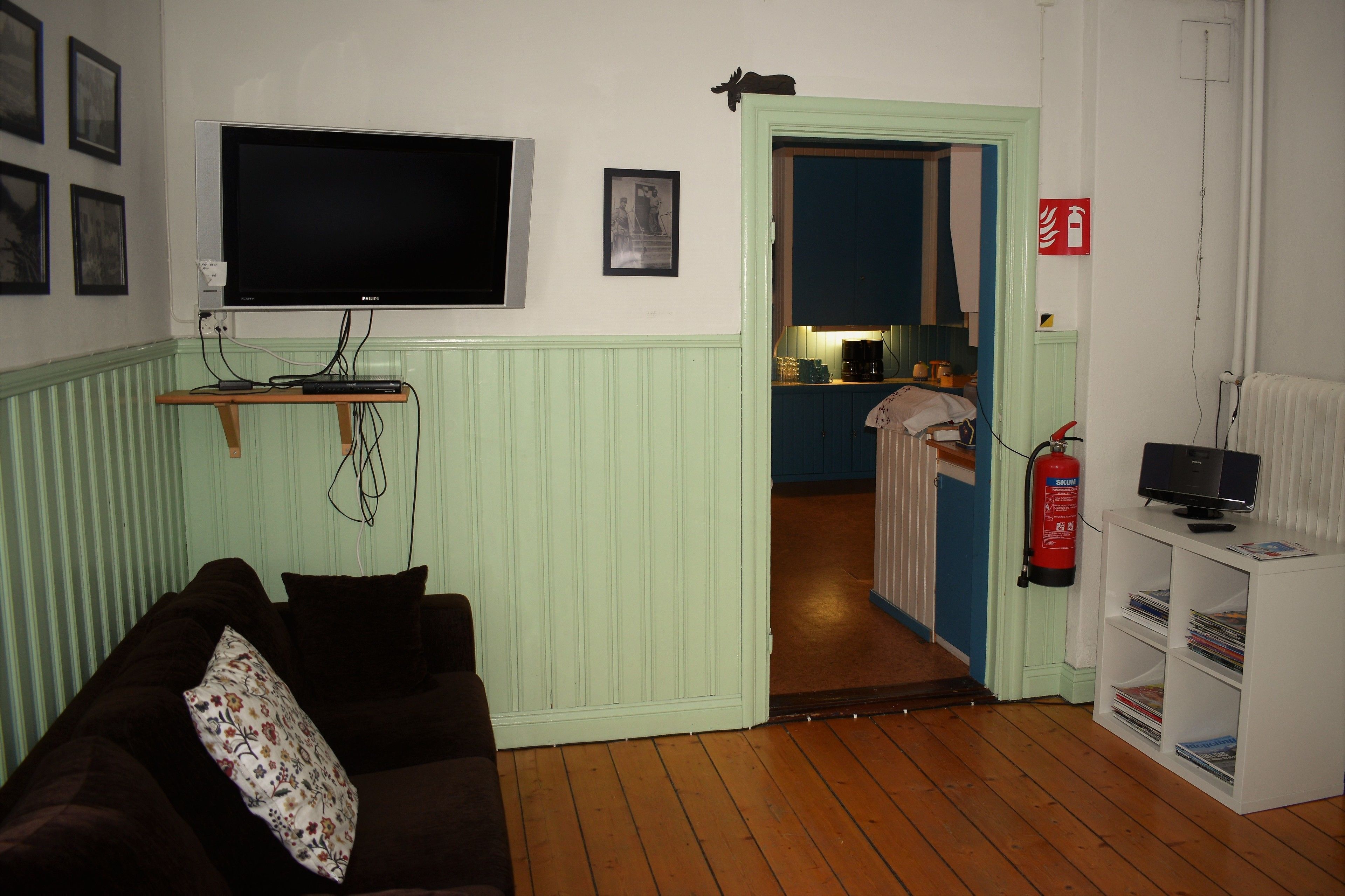 Un saló amb televisió, un sofà, una estanteria i una porta que dona a la cuina.