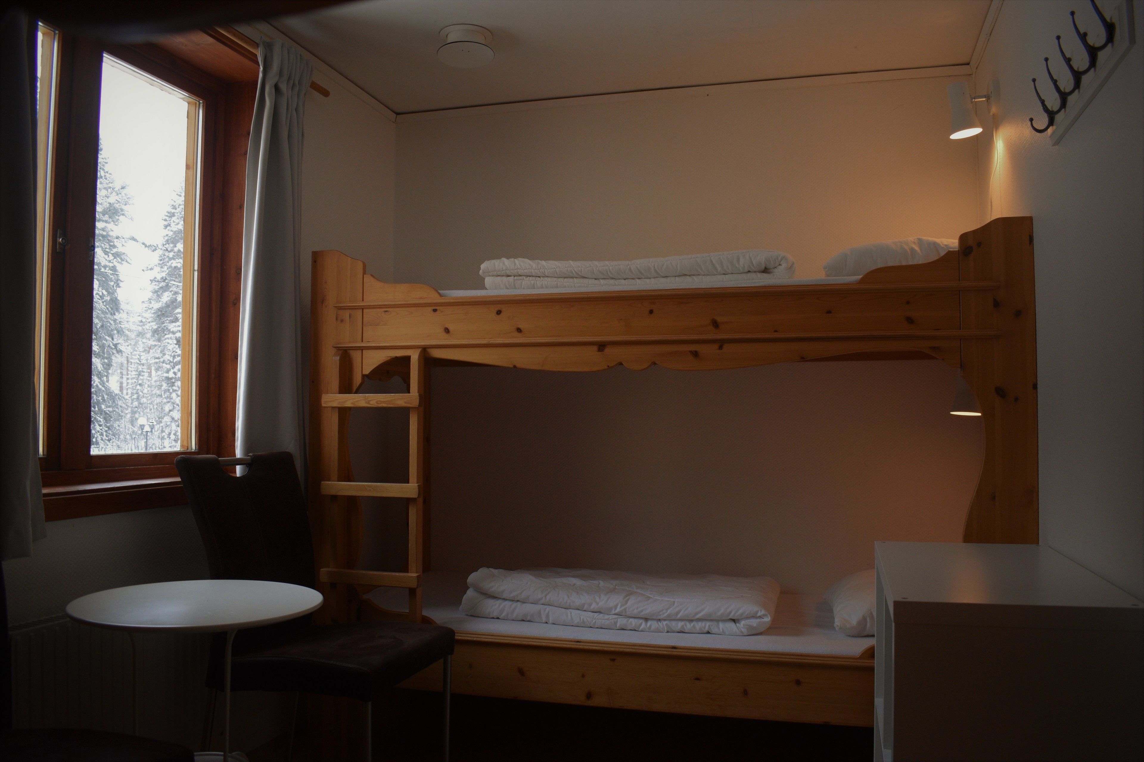 A bunk bed room with a window, a table, and a chair.