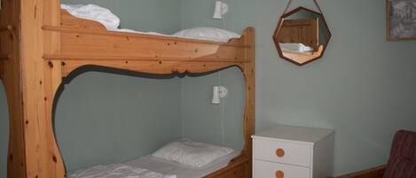 A bunk bed with a white mattress and pillows, a white dresser with drawers, a hanging mirror, and a framed picture on the wall.