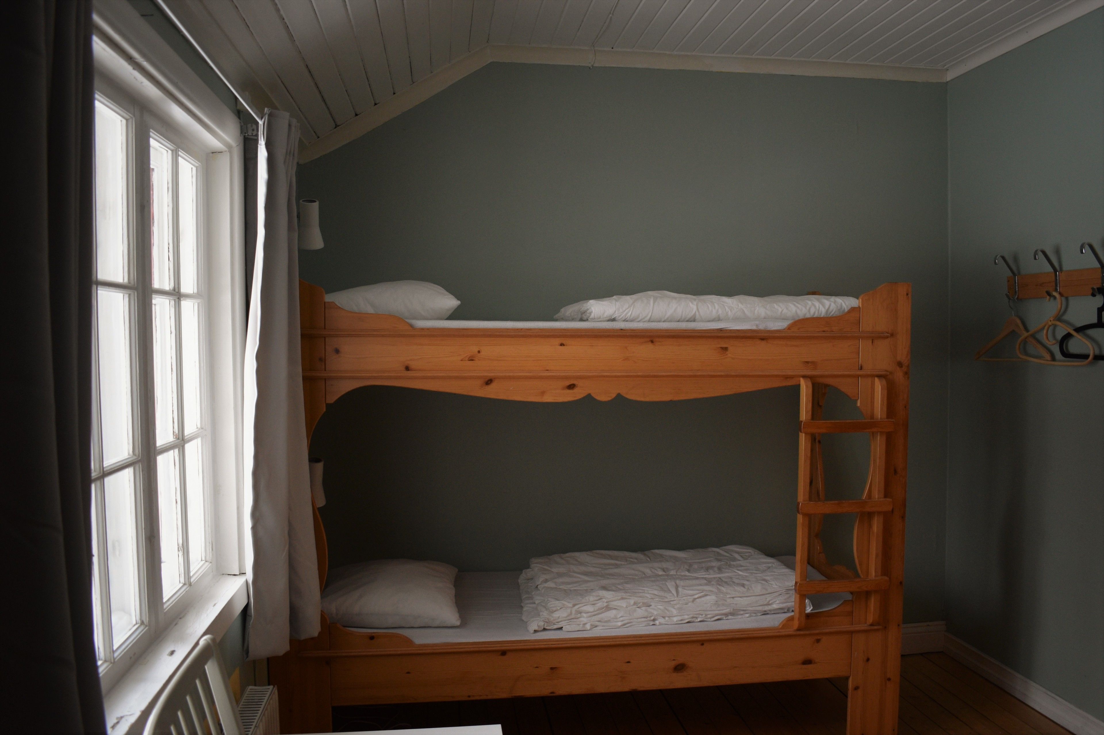 Una cama litera en una habitación con ventana, radiador y perchero.