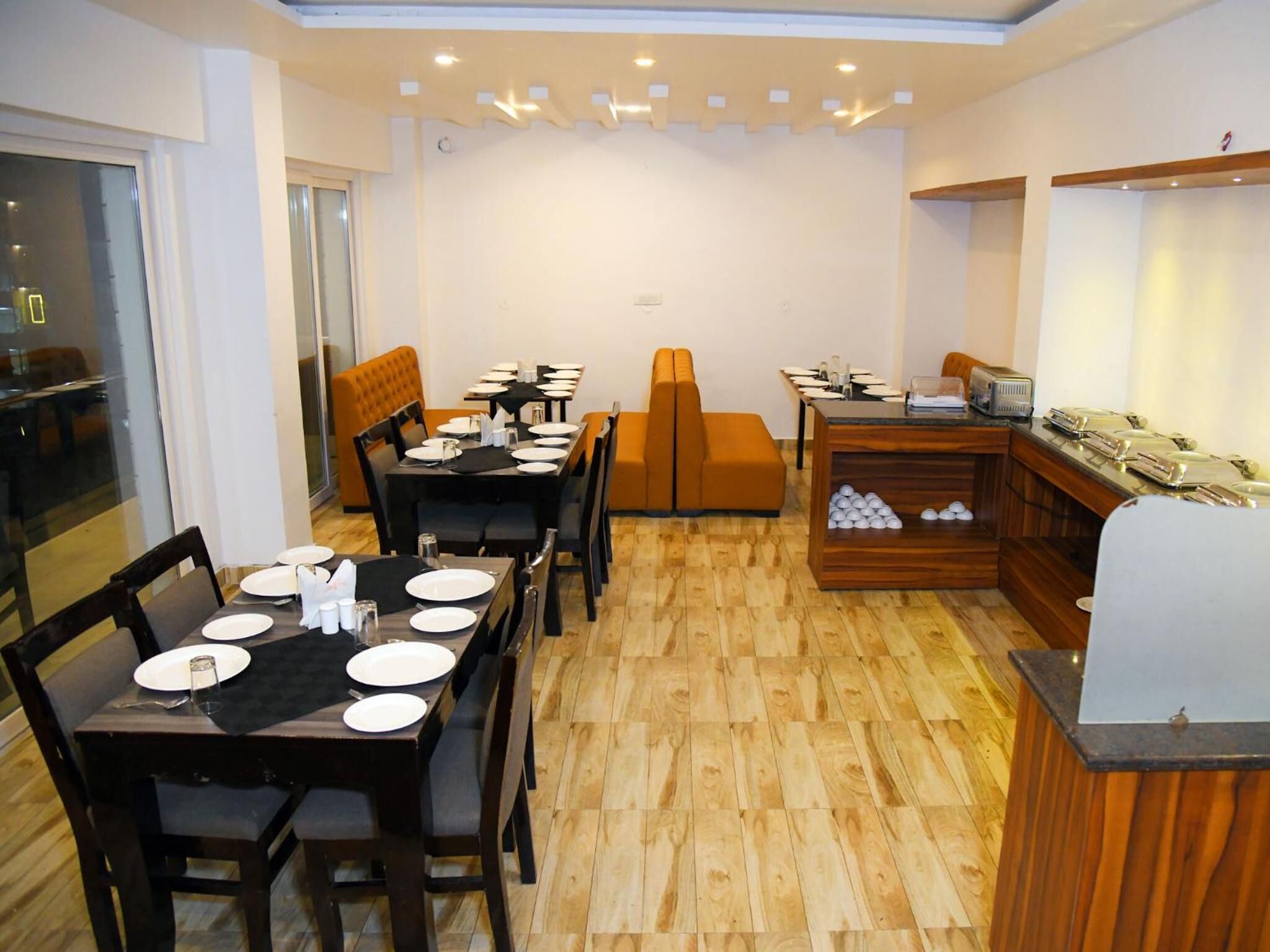 A dining area with wooden flooring, tables set with plates and cutlery, and a buffet station with a wooden counter and food items.