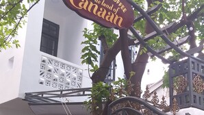 A sign for 'Homestay & Coffee The land of Canada' hanging from a tree, a decorative gate, and a building facade with a patterned entrance. - The Land of Canaan (Da Nang)