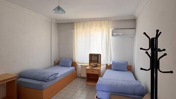 A small, clean room with two single beds, a sofa, a table, and a coat rack.