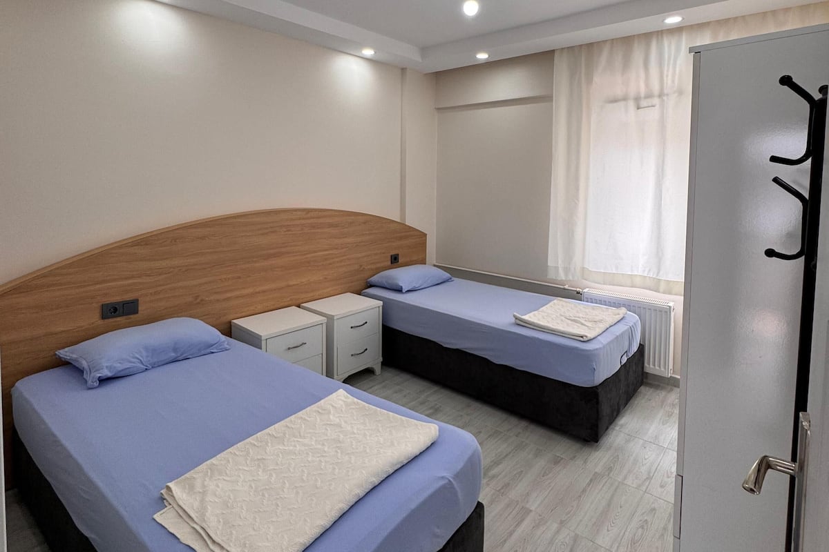 A hotel room with two beds, a wardrobe, a radiator, and a window with curtains.