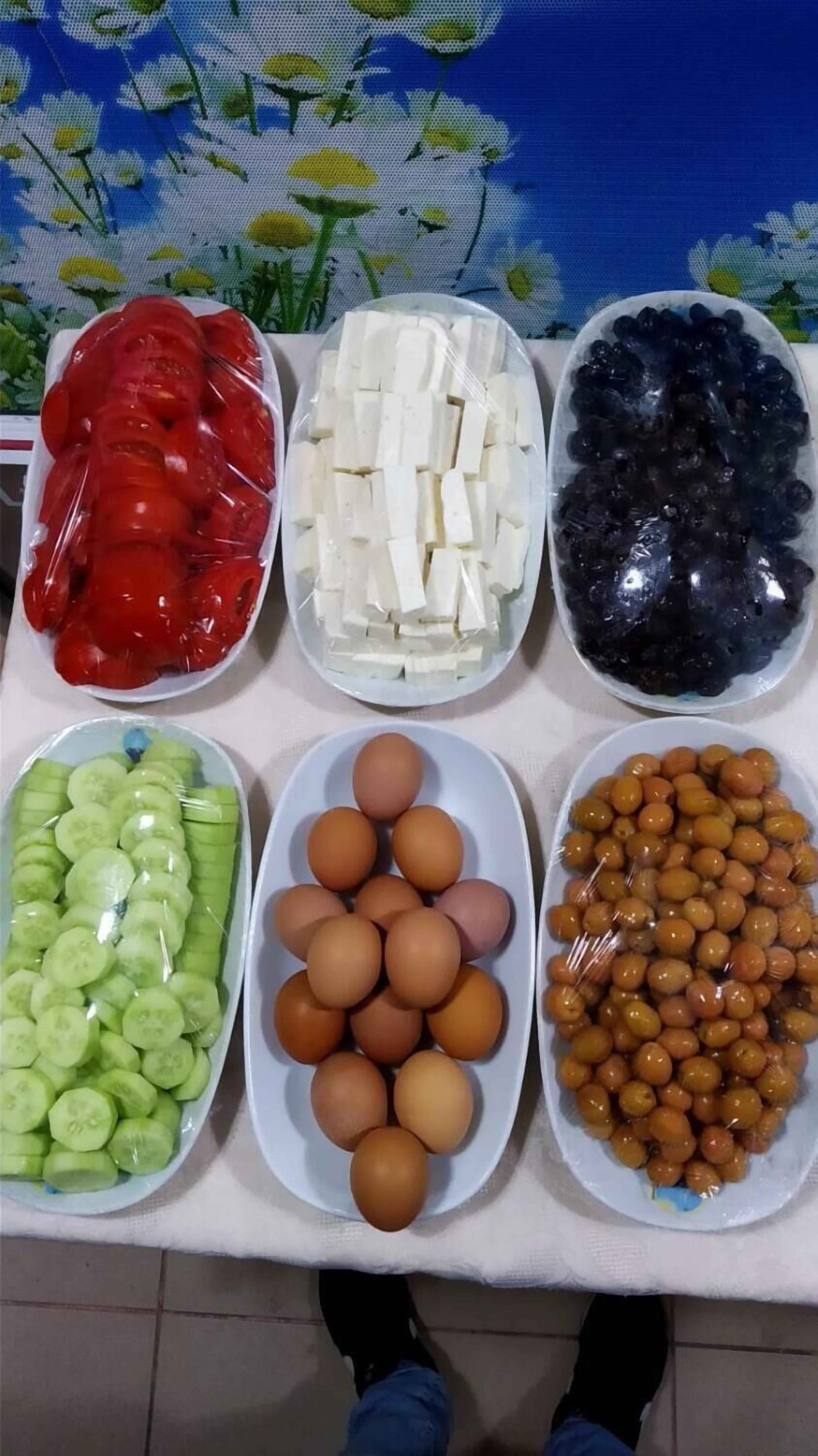 A table with various food items including tomatoes, tofu, black beans, cucumbers, eggs, and olives.