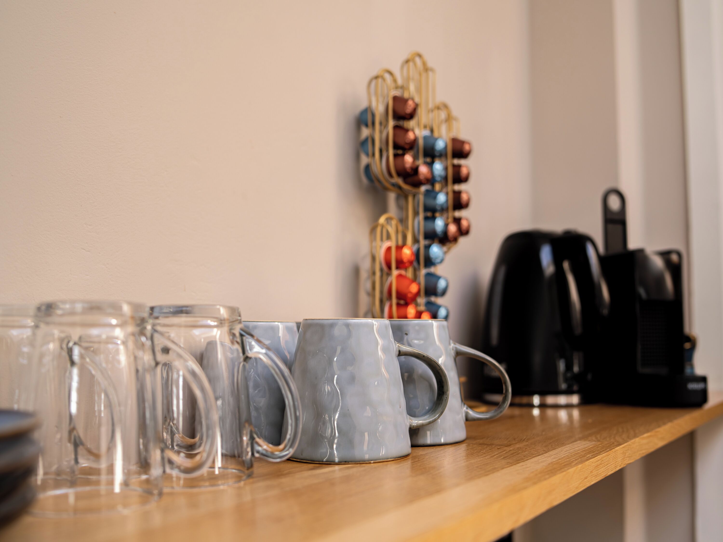 A kitchen counter with clear glass mugs, a coffee maker, and a spice rack.