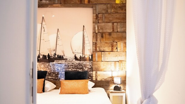 Un dormitorio con cama, almohadas, una mesita de noche y un mural de temática náutica en la pared.
