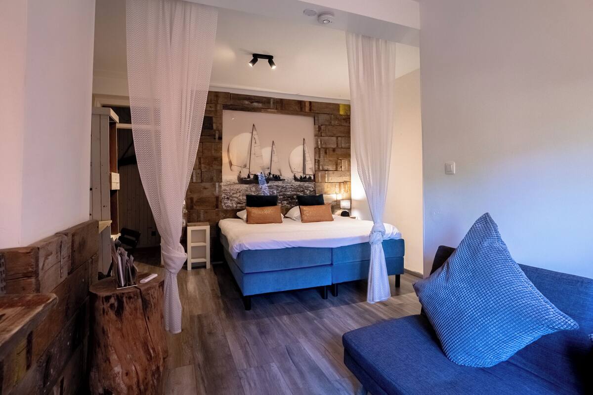 Un dormitorio con cama, sofá azul, pared de madera y ventana con cortinas.