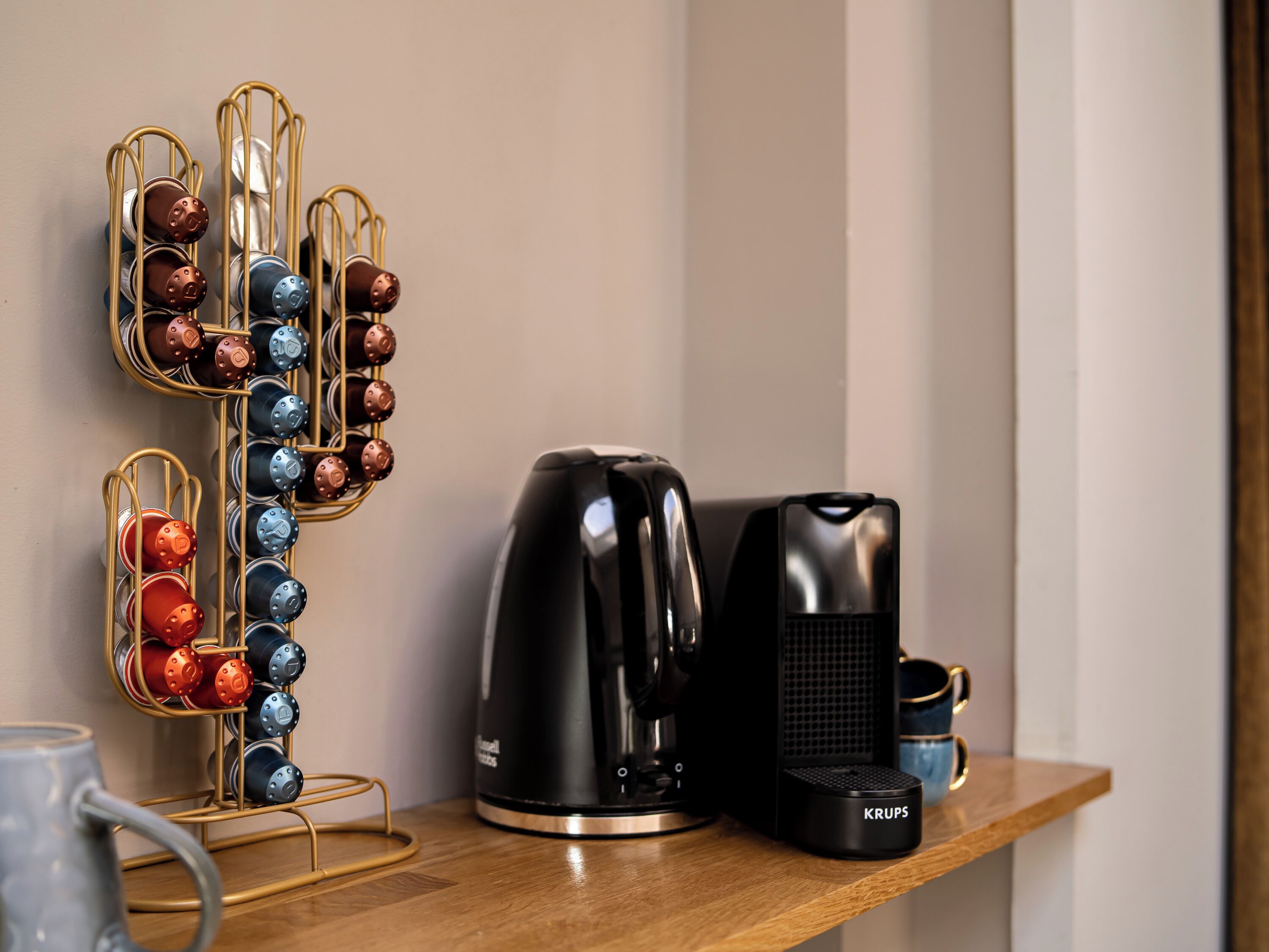 A coffee maker, a mug, and a metal rack with multiple mugs on a wooden surface.