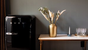 Una cafetera negra sobre una mesa de madera con un jarrón dorado que contiene plantas secas, una vela y varios vasos de vidrio.