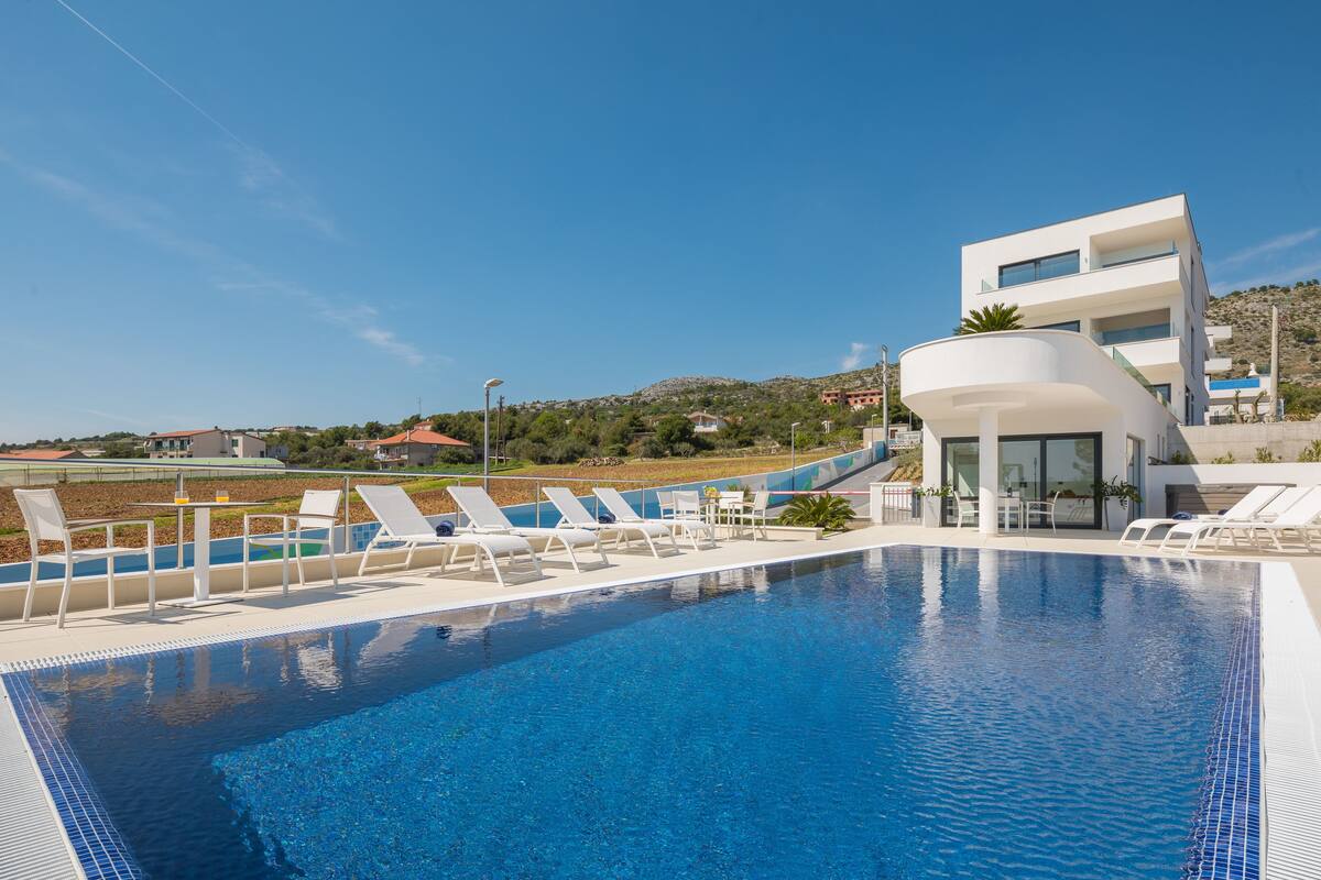A modern pool area with lounge chairs and a clear blue pool, surrounded by a landscaped garden and a hillside in the background.