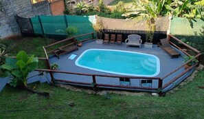A rectangular swimming pool with a wooden deck and seating area, surrounded by a fence and greenery. - Hotel Village del Sol (Puerto Iguazú)