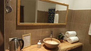 A bathroom with a wooden vanity, a large mirror, a sink, a kettle, and towels. - Hotel Village del Sol (Puerto Iguazú)