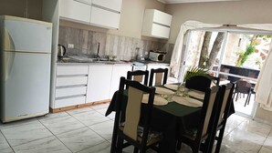 A compact kitchen with white cabinets, a refrigerator, and a dining area with a table and chairs. - Hotel Village del Sol (Puerto Iguazú)