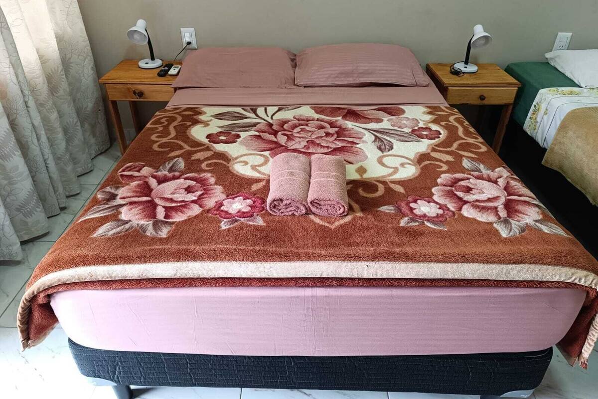 Ein ordentlich bezogenes Bett mit floralem Überwurf und zwei Nachttischlampen auf Holznachttischen.