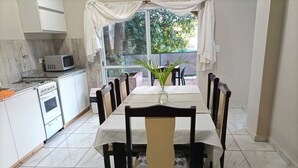 A dining area with a table set for six, surrounded by chairs, a microwave, and a stove in the adjacent kitchen. - Hotel Village del Sol (Puerto Iguazú)