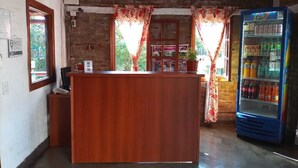 A reception area with a wooden counter, a blue beverage vending machine, and a window with curtains. - Hotel Village del Sol (Puerto Iguazú)