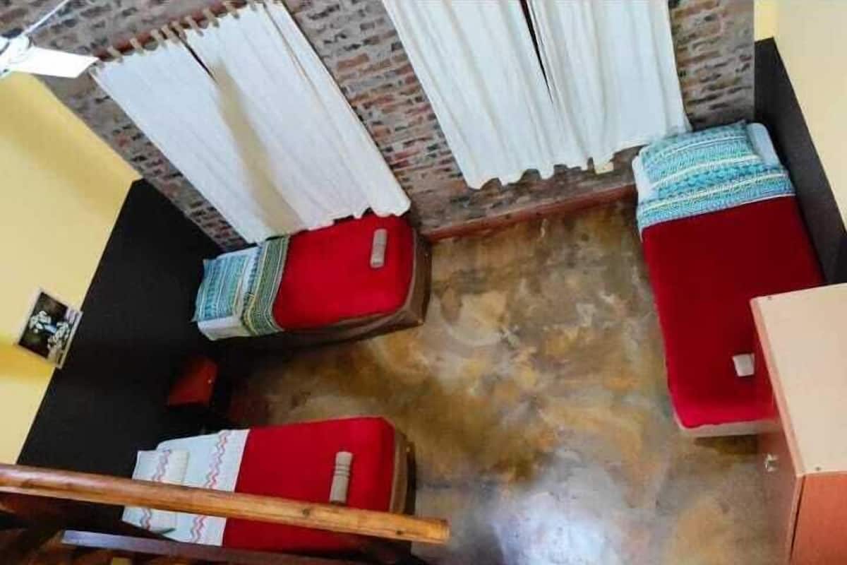 Ein Zimmer mit einer Holztreppe, einem roten Sofa, einem weißen Vorhang und einem gemusterten Kissen.
