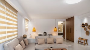 A modern living room with a sofa, coffee table, pendant lights, and a wooden cabinet. - Pebble Luxury Suite by the Sea (Hersonissos)