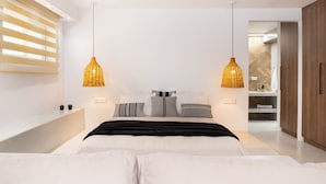 A modern bedroom with a large bed, two pendant lights, a built-in bench, and a view into the bathroom. - Pebble Luxury Suite by the Sea (Hersonissos)