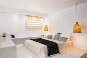 A modern bedroom with a large bed, bedside tables, and a window with blinds. - Pebble Luxury Suite by the Sea (Hersonissos)