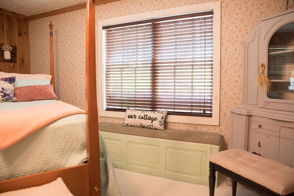 A bedroom with a bed, a window with blinds, a bench, and a dresser.