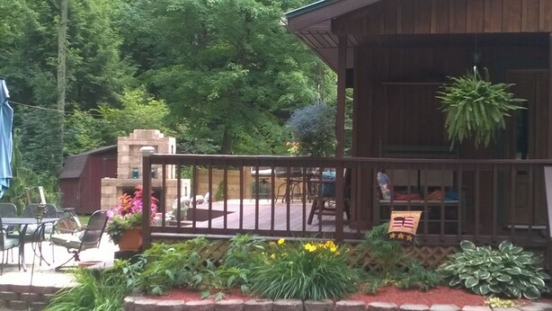 A wooden building with a balcony, outdoor seating, and a stone structure in the background. -  Cottage in the Woods- "Hummingbird"-- 2mi from Ricketts Glen falls trailhead! (Sweet Valley)
