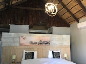 A bedroom with a wooden headboard, a large painting, and a unique circular light fixture. - Thomo's Inn (Maun)