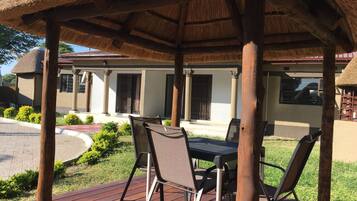 Relax in a shaded outdoor space with a thatched roof, metal chairs, and a table for dining or socializing.
