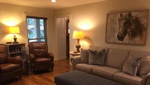 A living room with a leather armchair, a sofa, and an ottoman. There is a bookshelf and a painting on the wall. - Natchez Trace Cabin Retreat on 5 acres (Canton)